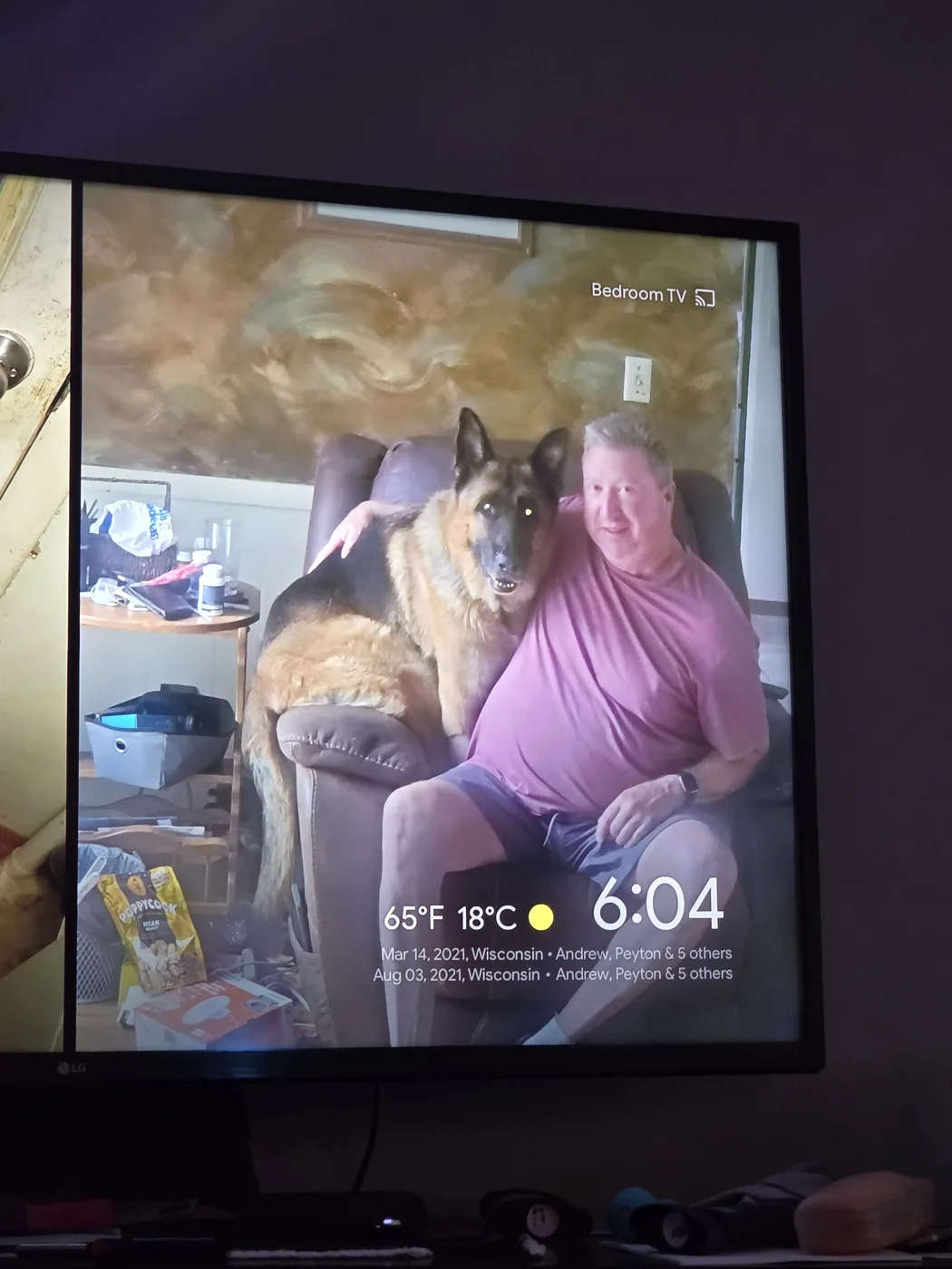 The man-and-dog recliner photo displayed as a TV screensaver, timestamped 6:04